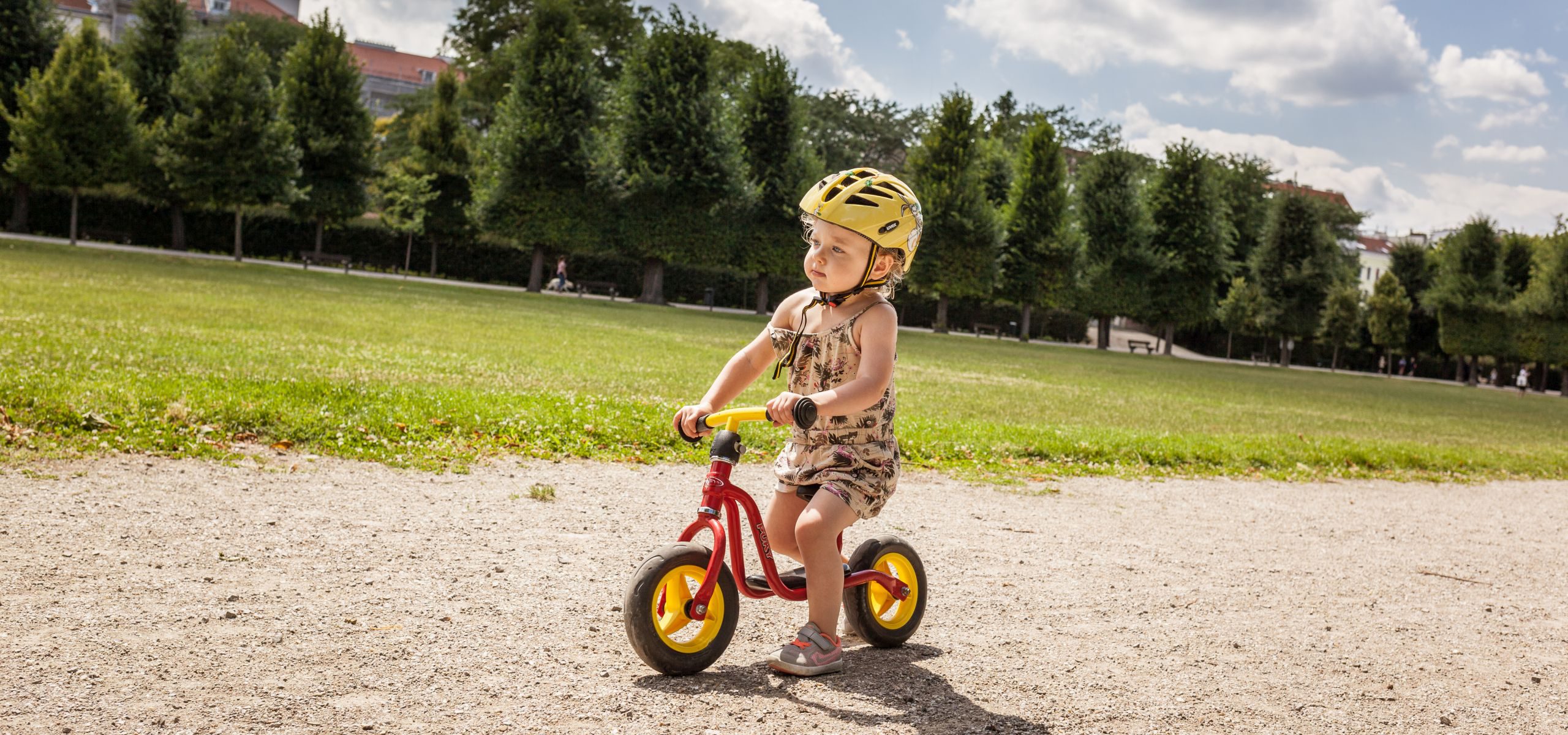 Kleines blondes Mädchen fährt mit einem Laufrad im Augarten.